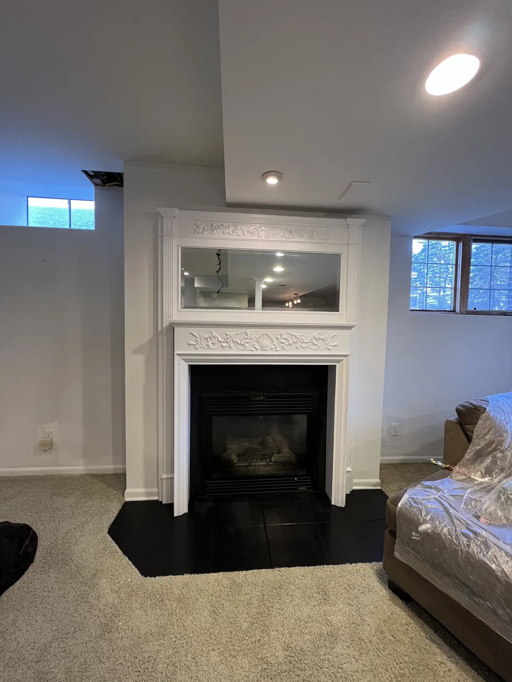 A living room with a tall white fireplace surround and a picture window above it.