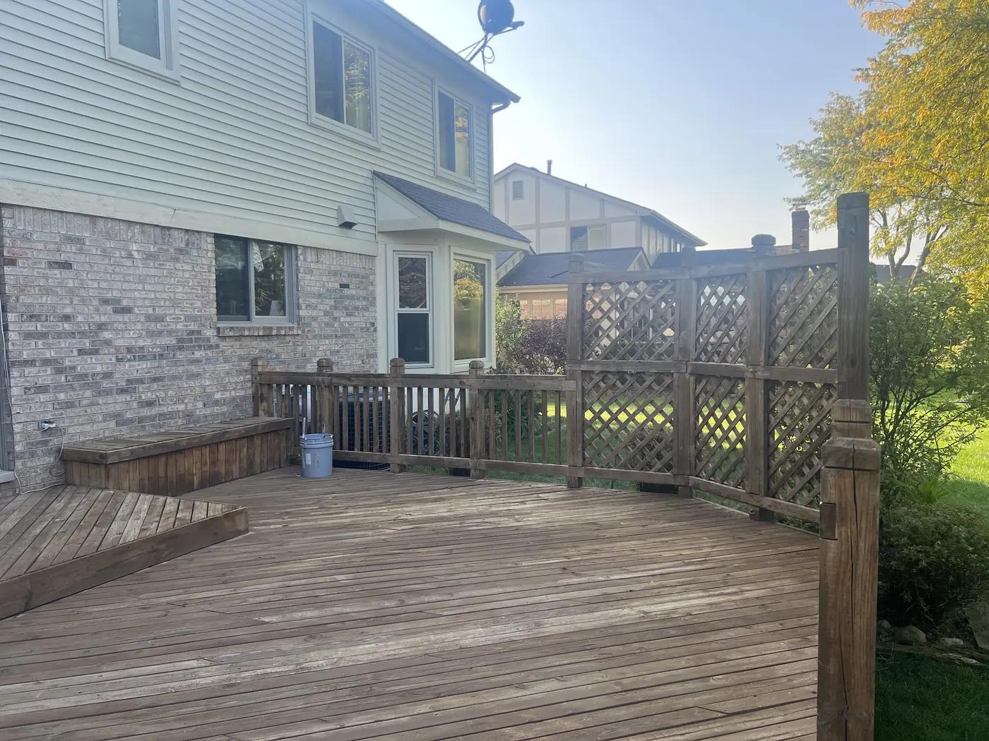 A backyard deck with grey, weathered boards and a bare lattice privacy screen before any finish is applied.