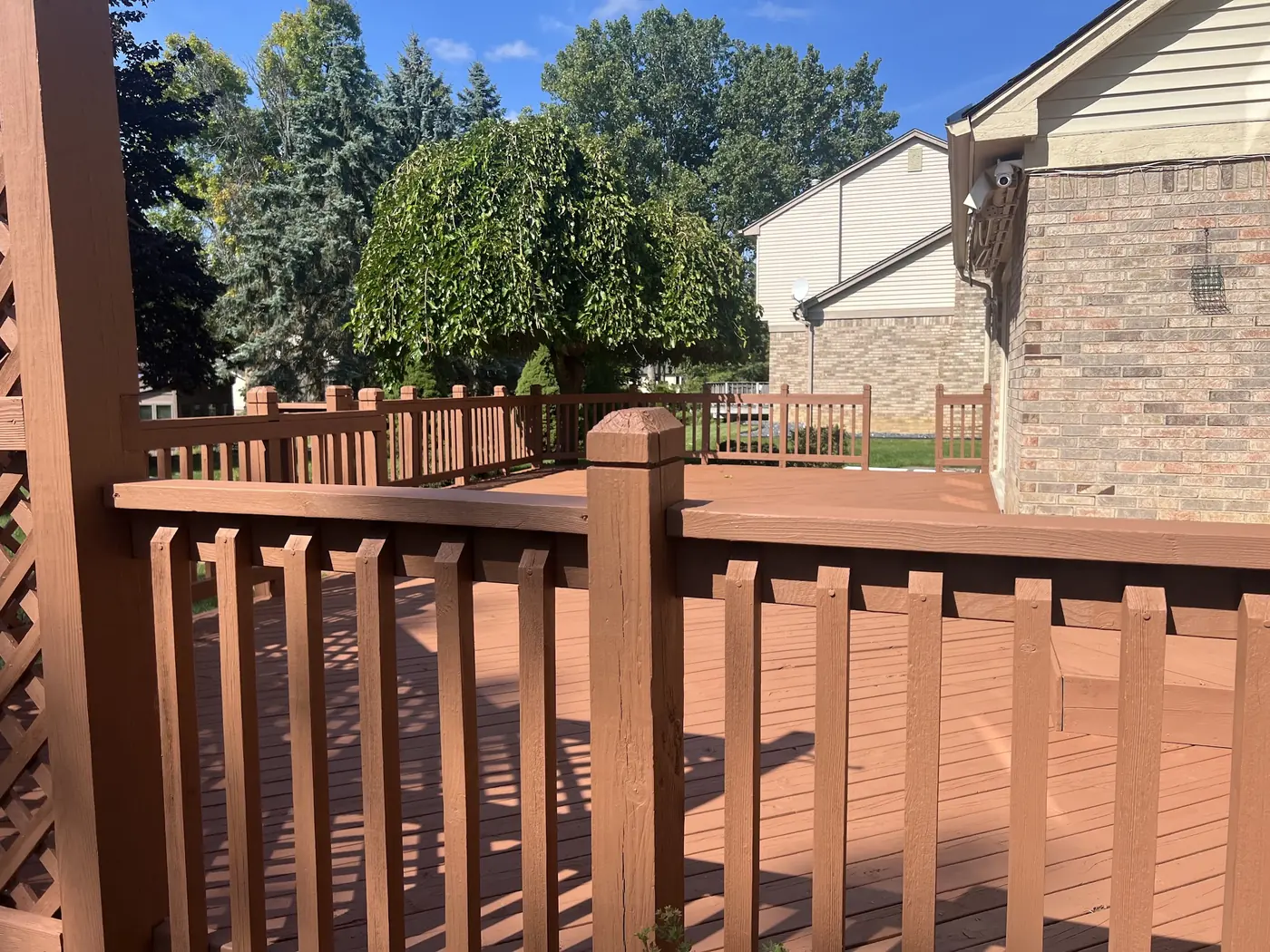 A finished deck, railings and posts evenly stained, with the brick of the house alongside.